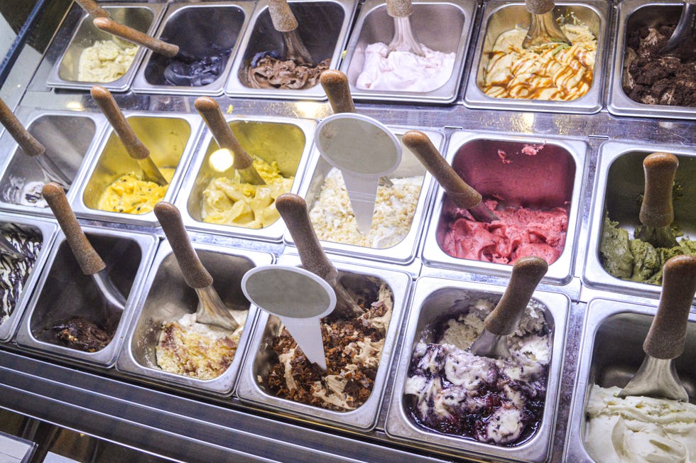 Variety of ice cream flavors in metal containers with serving scoops