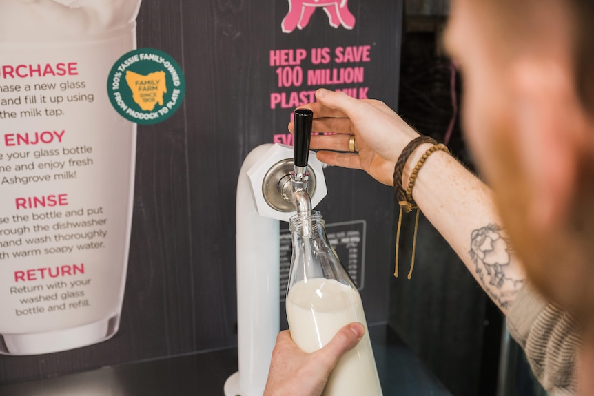 A person fills a glass bottle with milk from a refillable keg.