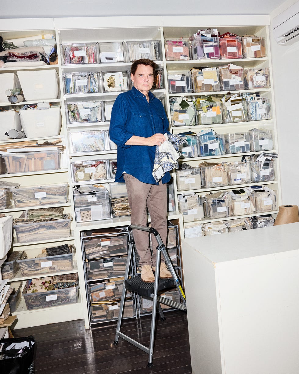 Person standing on a step ladder in front of organized shelves filled with fabric samples.