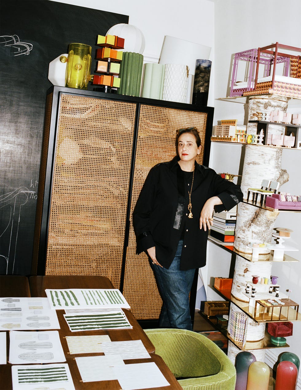 Person in a studio surrounded by colorful models and design sketches on a table.
