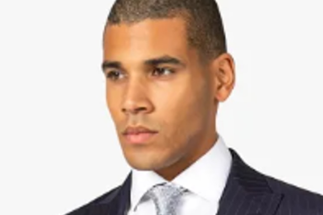 Elii Emeghebo wears a dark suit jacket, white shirt and silver tie.