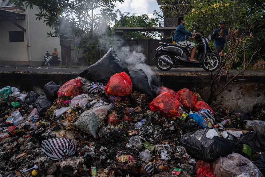 A man on a bike drives by a mountain of rubbish.