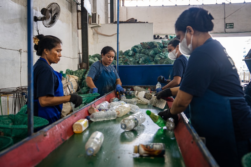 A group of four women sorts through plastic bottles at a recycling centre.