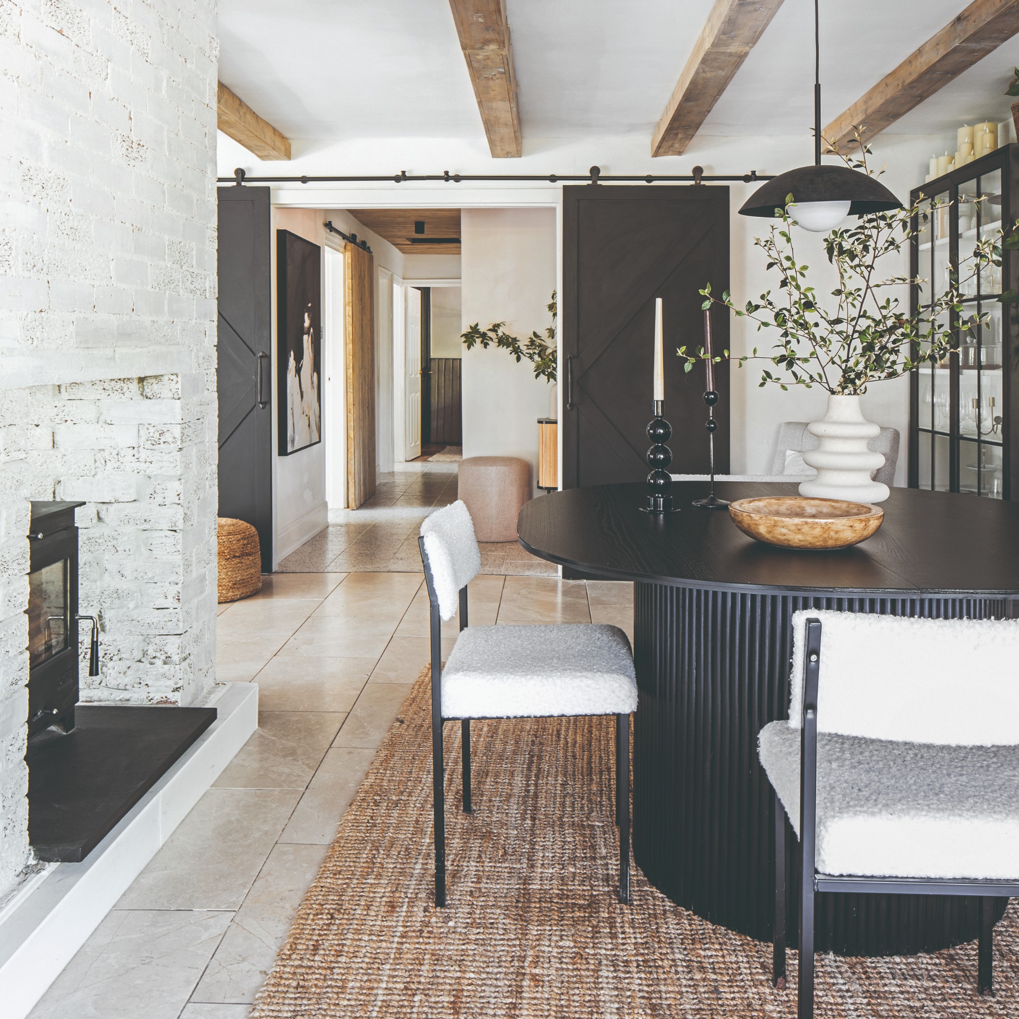 An open-plan dining area with a round black dining table with white boucle dining chairs on top of a jute rug