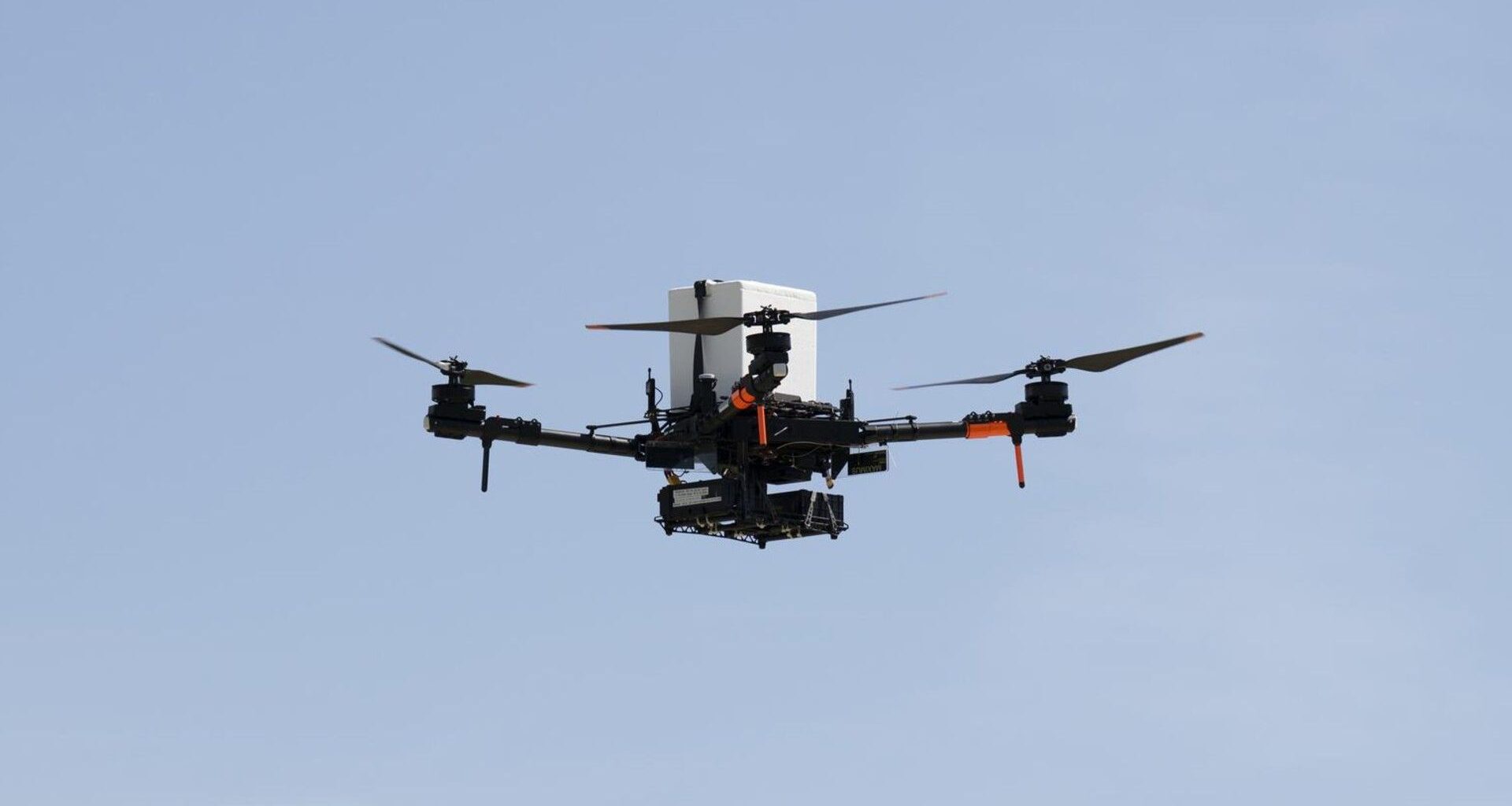a large quadcopter drone flies in front of a clear, blue sky