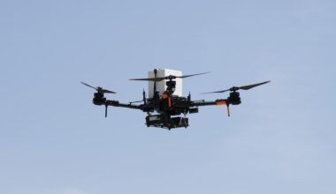 a large quadcopter drone flies in front of a clear, blue sky