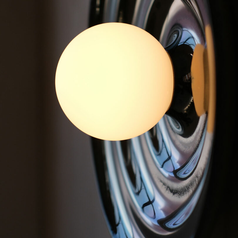 A round light bulb illuminated against a reflective metallic surface, capturing its glow and reflections.