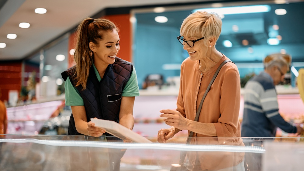 woman wearing a ponytail presenting a product to another woman with shorter hair on a supermarket