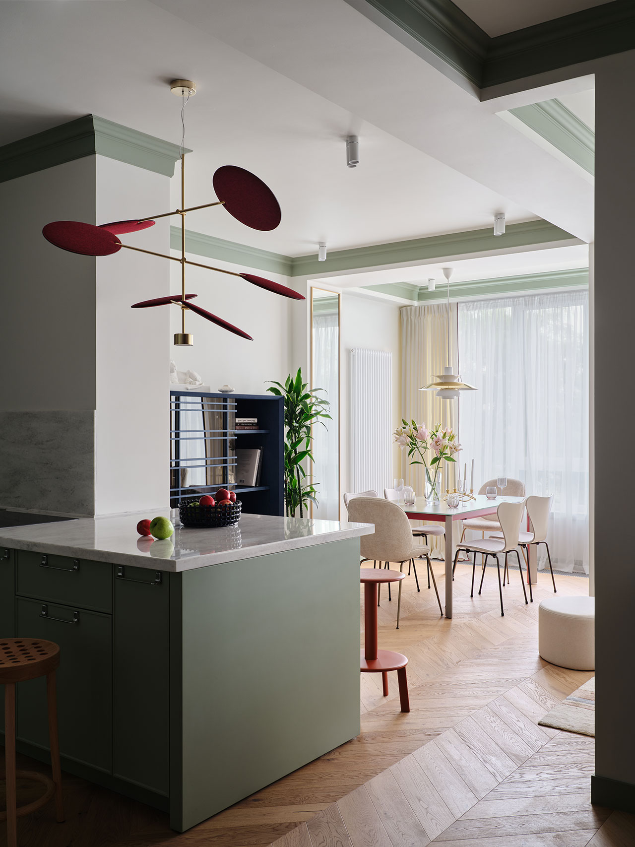 Modern kitchen with a green island, marble countertop, and a dining area with round table and chairs by large windows with sheer curtains.