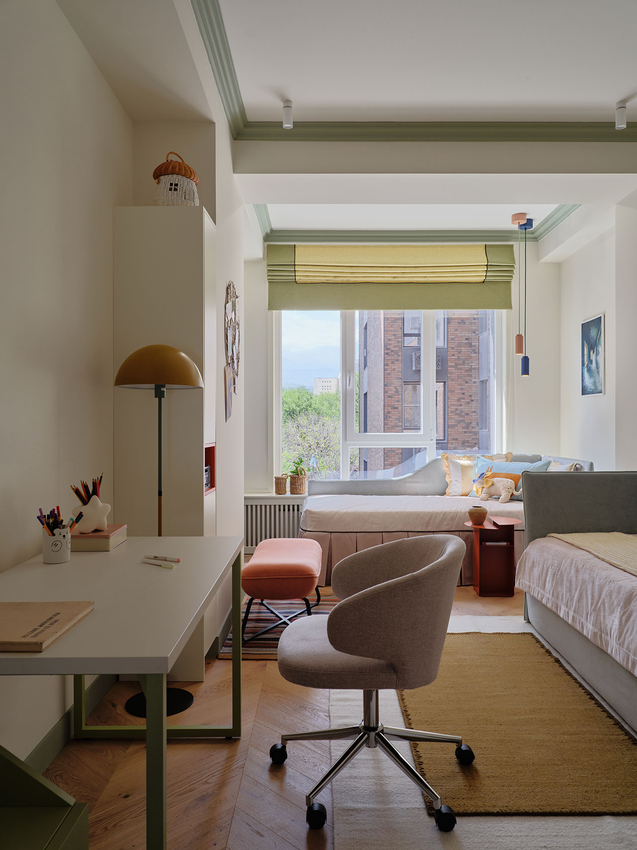 A tidy bedroom with a desk, chair, bed, and large window with a green shade, featuring neutral and pastel colors, wooden flooring, and some decor items.