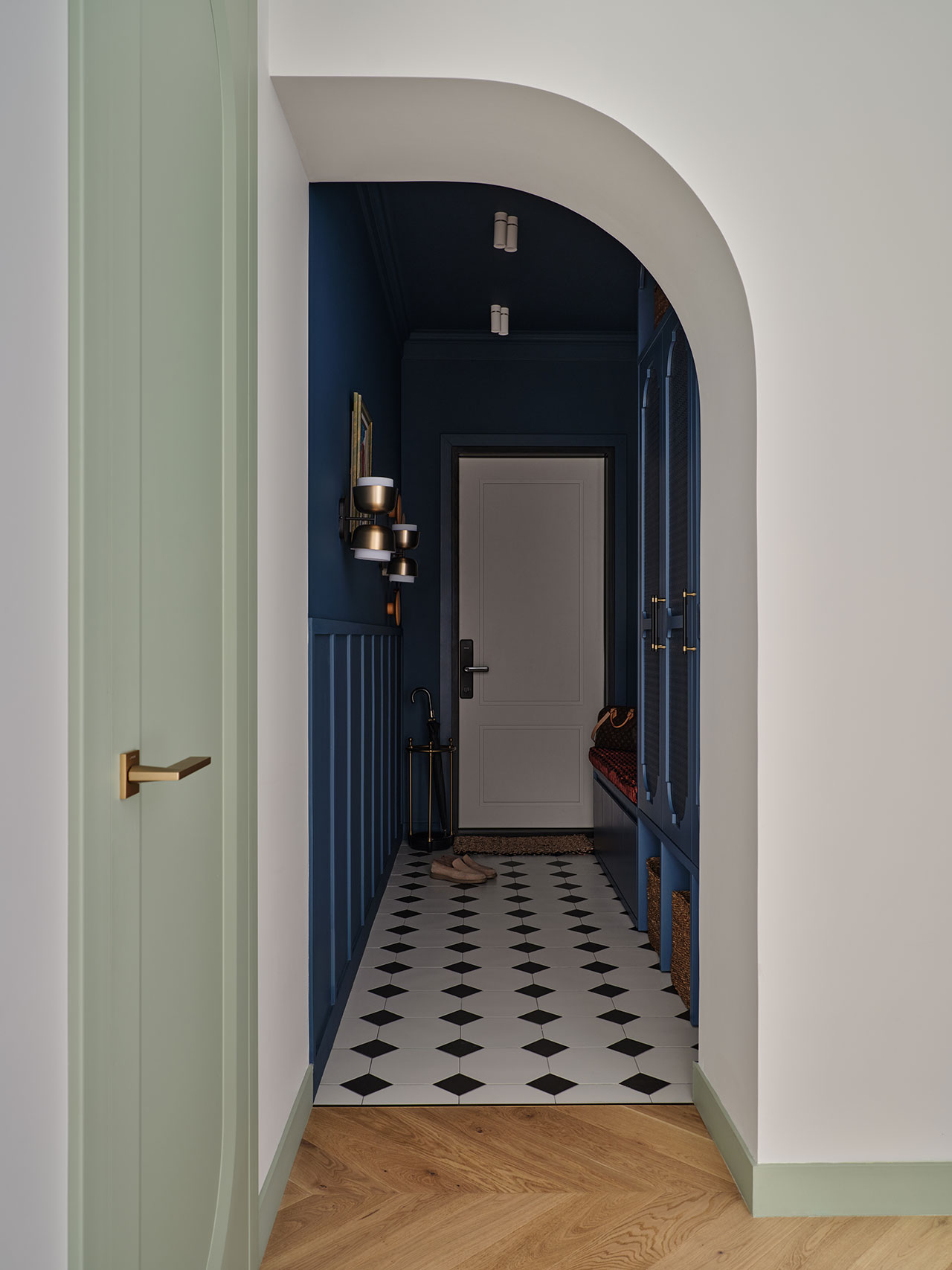 A hallway with a white door, dark blue walls, black and white checkered floor tiles, and a light green arched doorway with a gold handle.