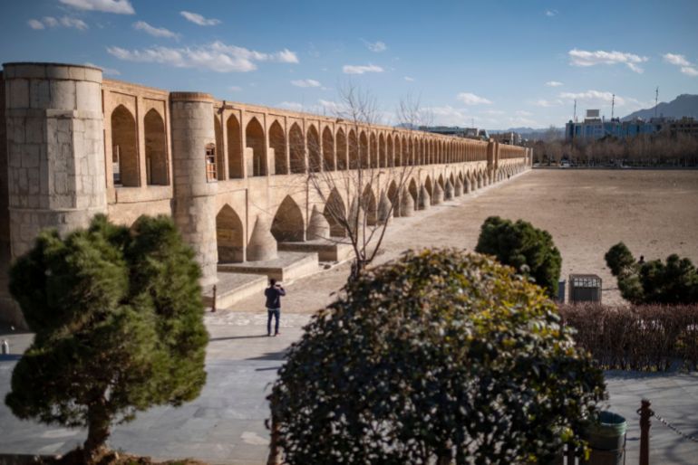 An Iranian man stands on the dried-up riverside of the Zayandeh Rud River as a view of the Si-o-se-pol (33-Bridge) historical bridge is pictured in the historic city of Isfahan, Iran, on February 22, 2025. Zayandeh Rud is one of the main tourist attractions of Isfahan, which has completely dried up. Historical bridges such as 33-Bridge on the river may be damaged due to subsidence of the Zayandeh Rud riverbed if the drought continues. (Photo by Morteza Nikoubazl/NurPhoto via Getty Images)