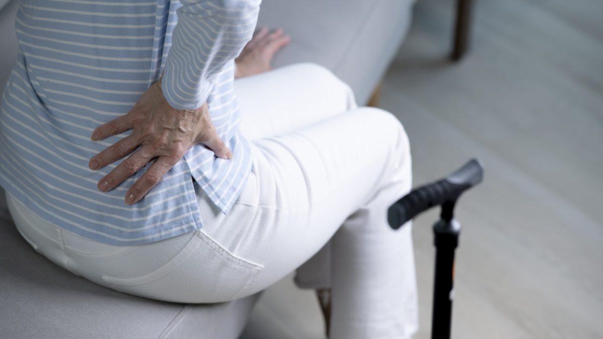 Senior woman on sofa feeling and suffering from back pain. - stock photo