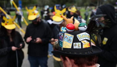 A player wearing a hat decorated with Pokemon characters and trading cards plays Pokemon GO on a smartphone during the in-person Pokemon GO Tour: Kalos Los Angeles 2026 event at the Rose Bowl Stadium in Pasadena, California, on February 20, 2026.
