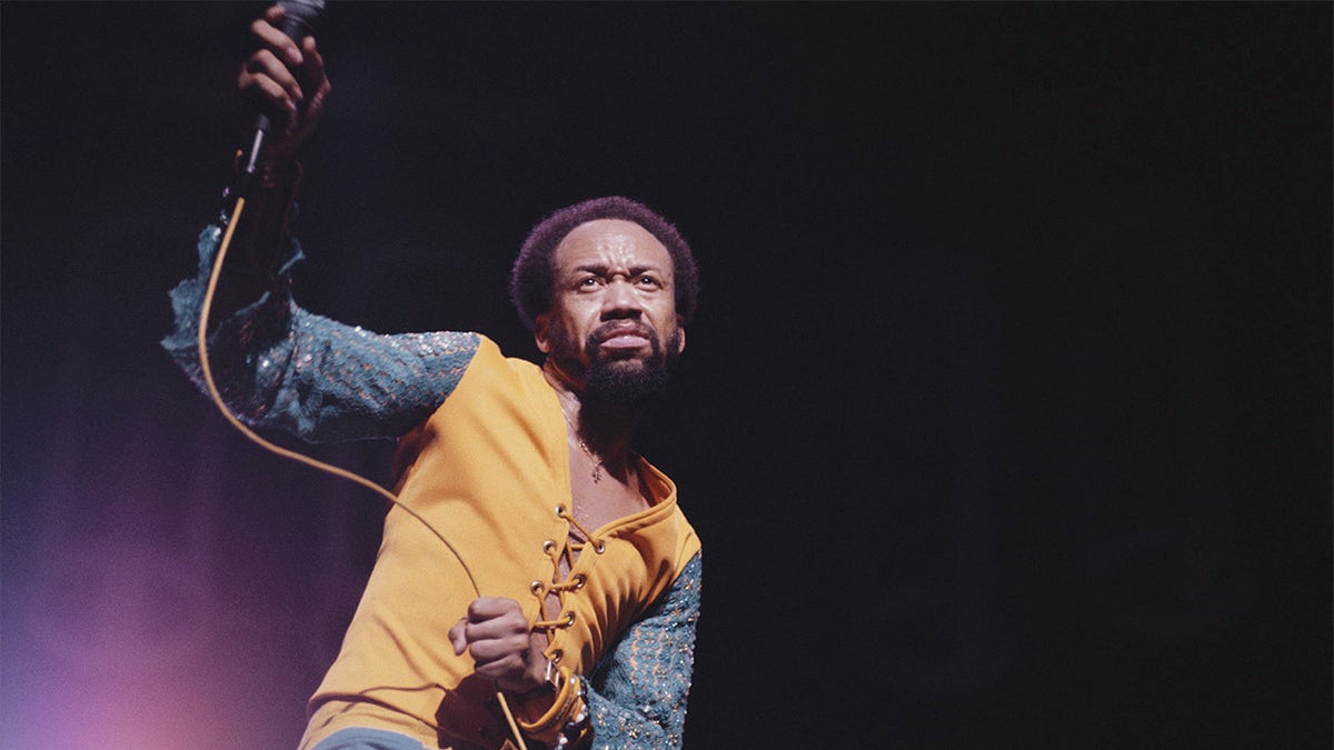 Maurice White singing and playing drums on stage.