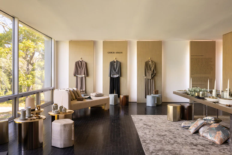 Modern showroom with elegant clothing displays and home decor, featuring neutral tones and large windows with a garden view.