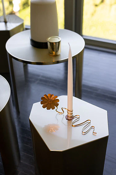 Modern gold candle holder with a twisted design on a hexagonal table near a window.