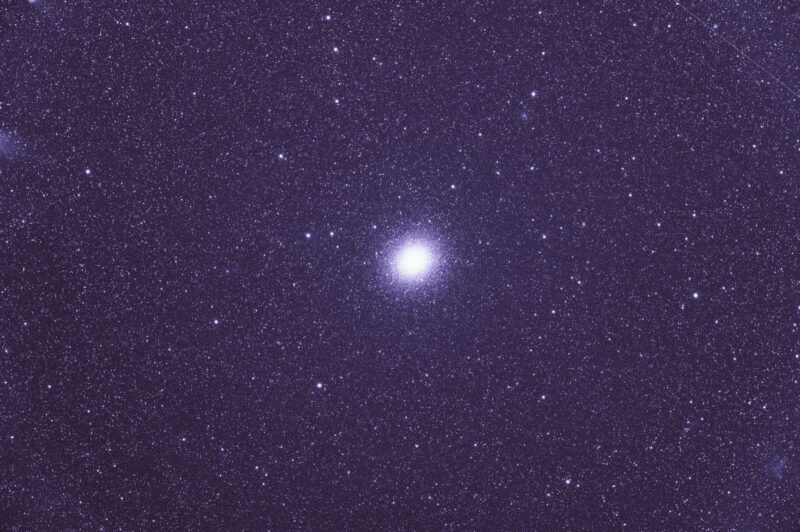 A large, spherical cluster containing thousands of bright white stars, located in a prolific star field.