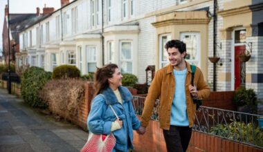 Front view of a young couple walking down terraced Street in Whitley Bay in the north-east of England they are heading into the town centre and deciding which shops to go to they are also holding hands and carrying bags over their shoulders.