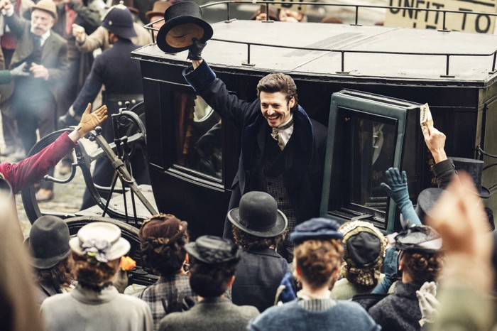 Guinness Anthony Boyle as Arthur Guinness, stepping out of a carriage to a crowd of people, wearing a suit, raising his hat