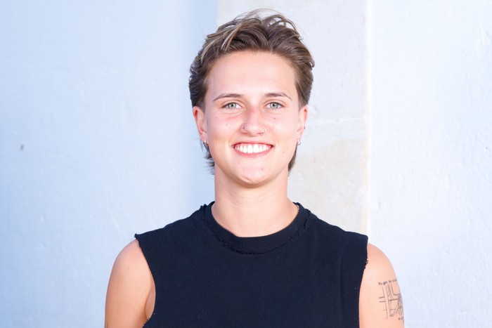 Elise smiling in front of a white background, wearing a blue vest top.