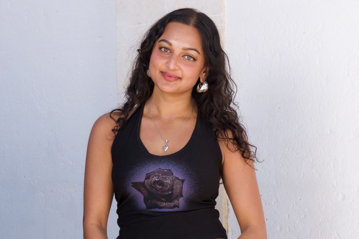 Nikita stood in front of a white background, wearing a black vest top.
