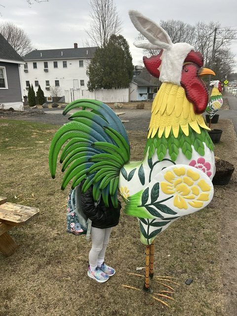 Pyper LaBlanc hides under the tail of an Easter-themed rooster before school in April 2025. (Courtesy of Dave LaBlanc)