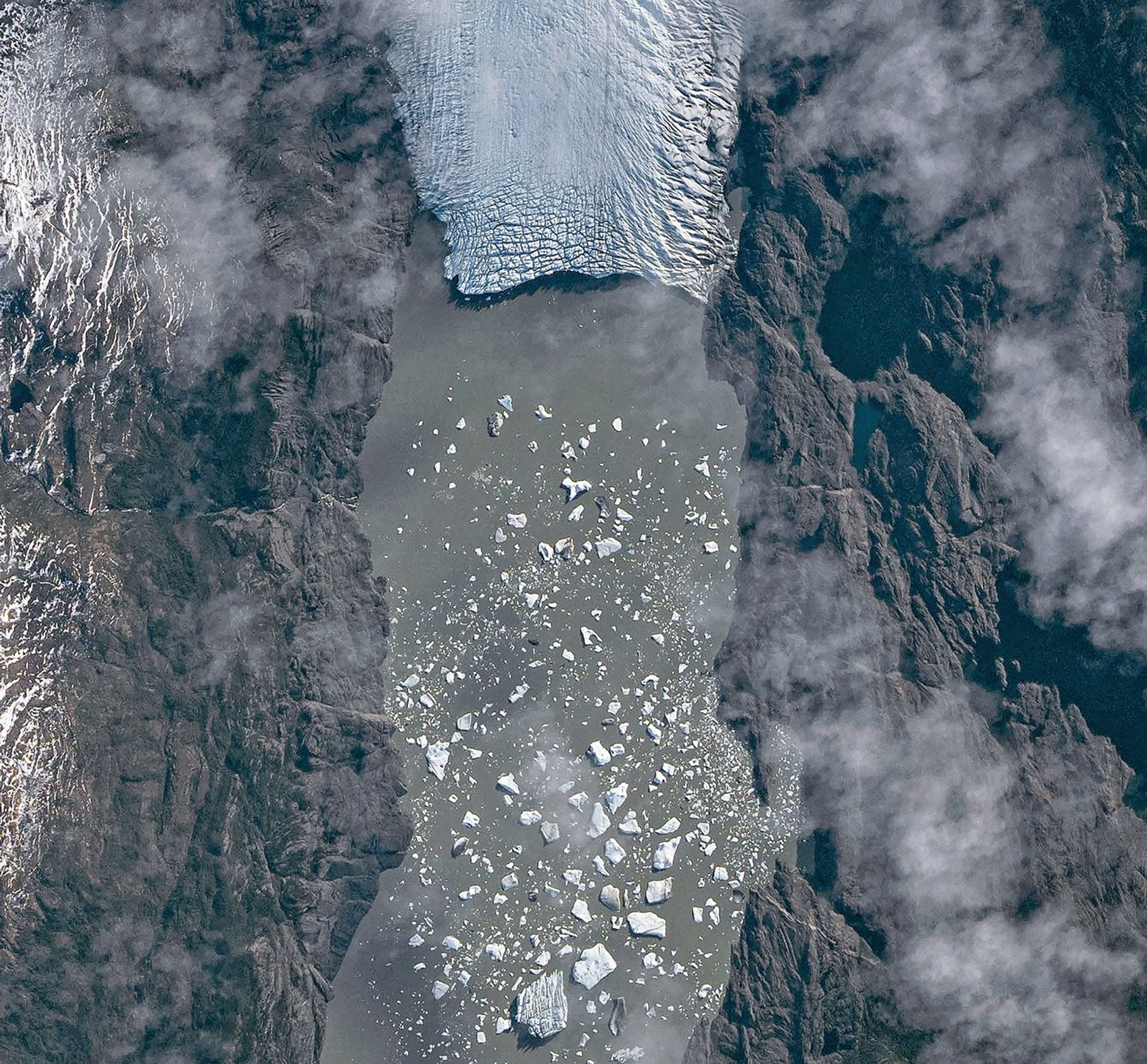 A top-down photo shows a detailed view of the leading edge of a glacier terminating in a lake. The glacial ice is heavily crevassed with intersecting linear features.