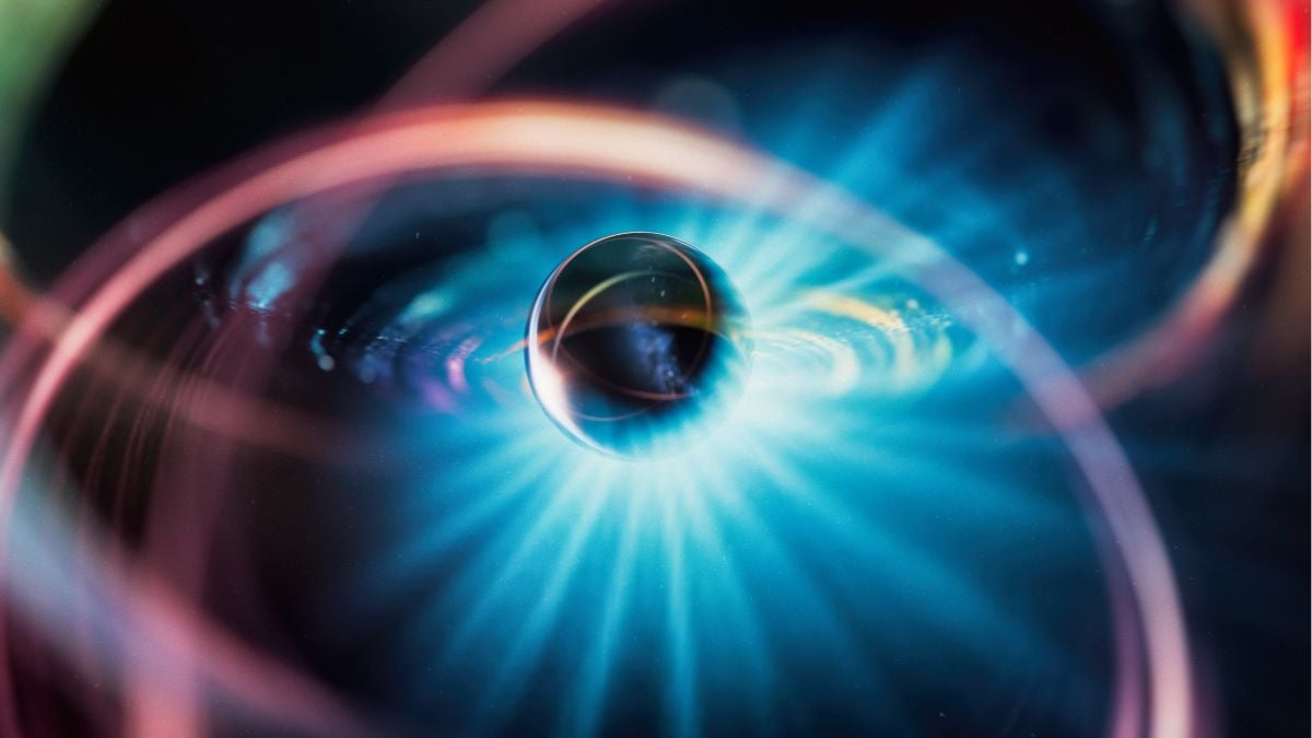 An abstract illustration of a dark sphere surrounded by a bright blue energy burst and pink orbit-like rings.