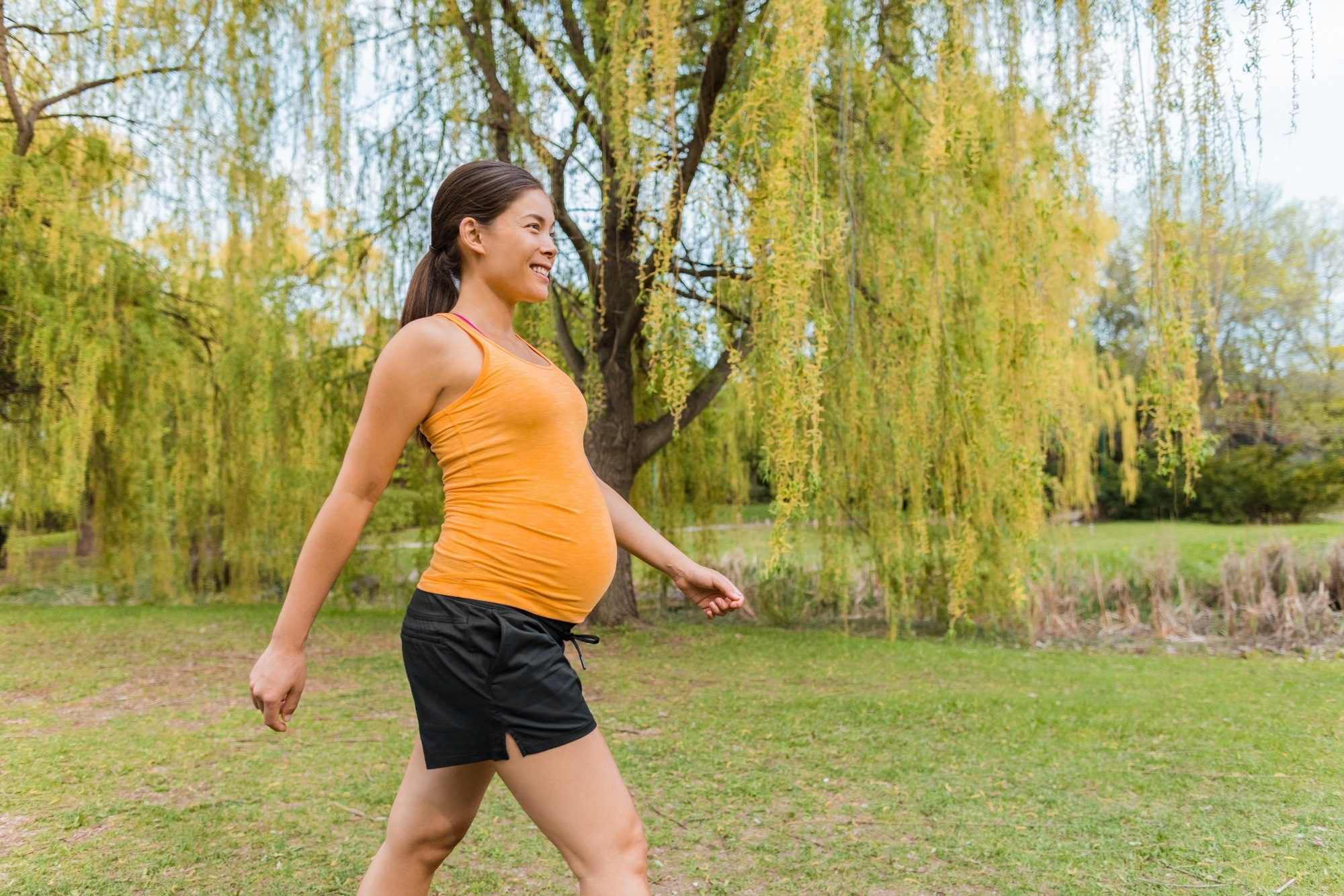 Pregnant woman walking outside in city park during summer for healthy active body workout