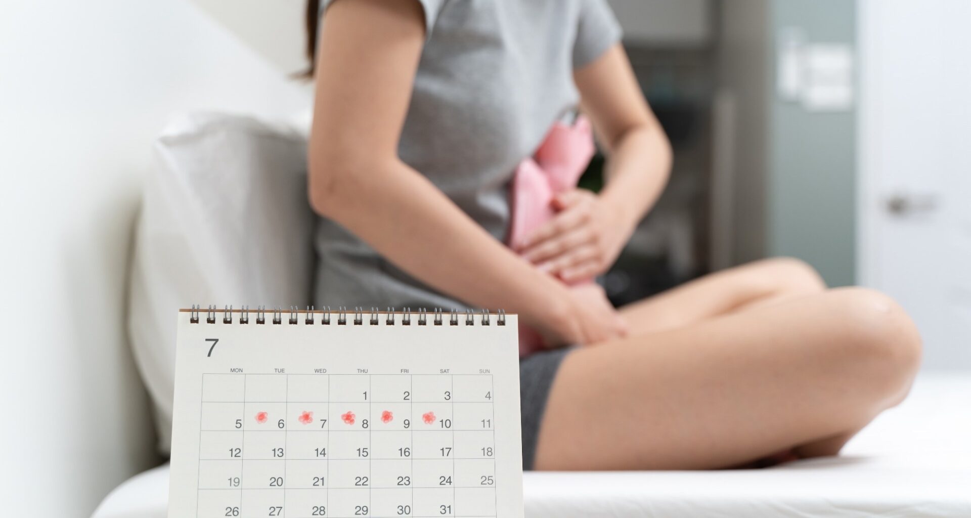 Close-up woman touching her belly and feeling stomach pain from cycle period on the bed at home.