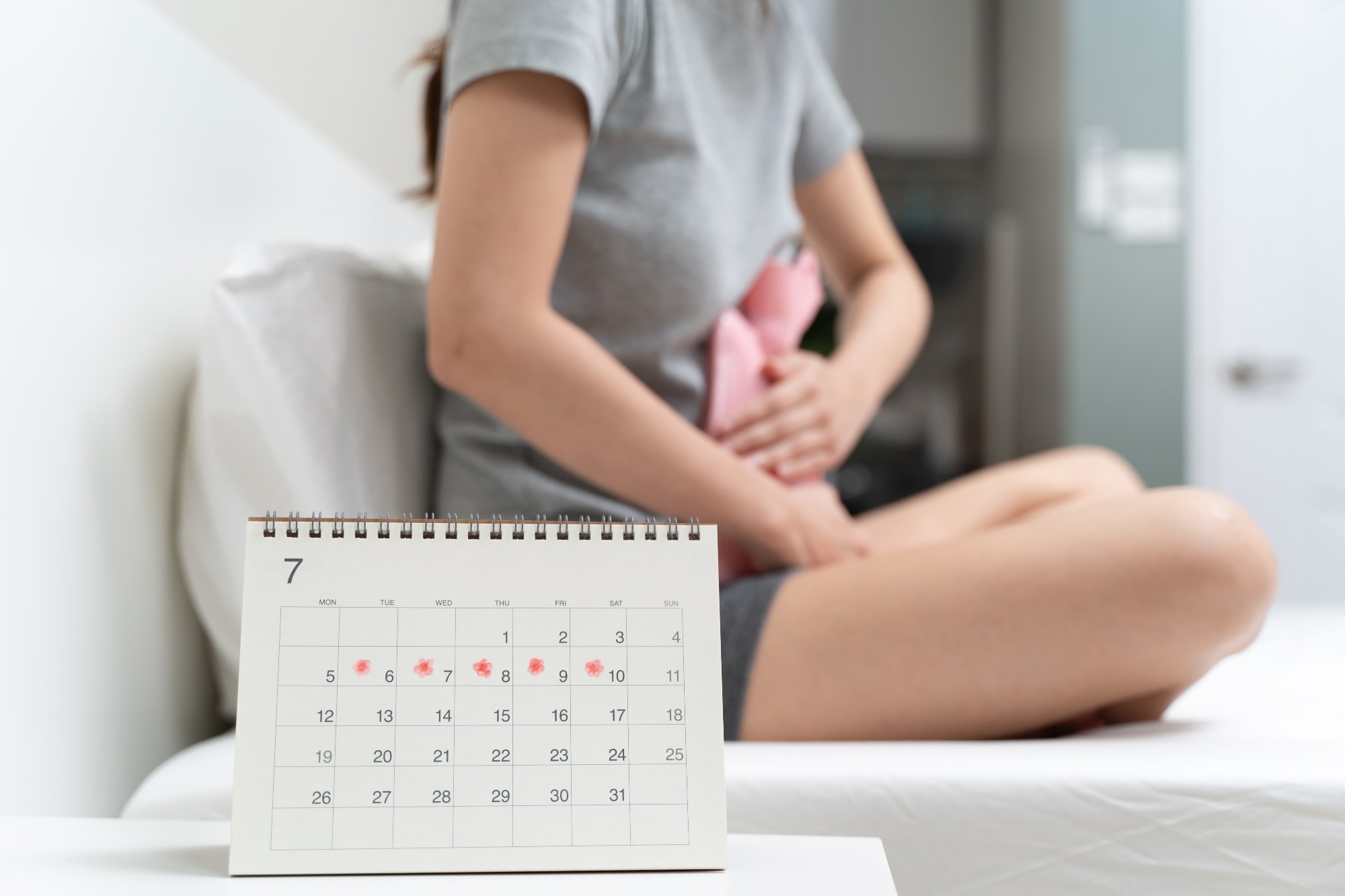 Close-up woman touching her belly and feeling stomach pain from cycle period on the bed at home.