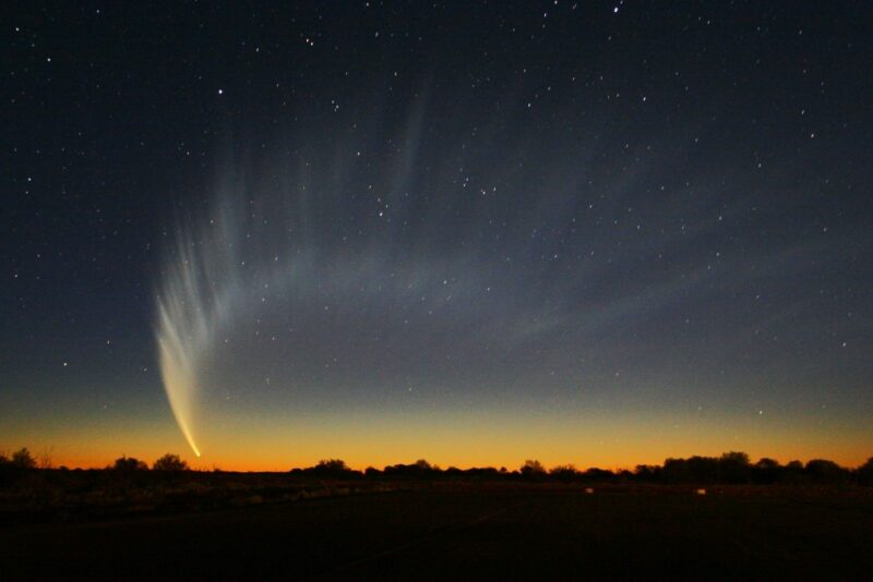 Passing star: Twilit-sky with a comet that has a diffuse, arching tail.