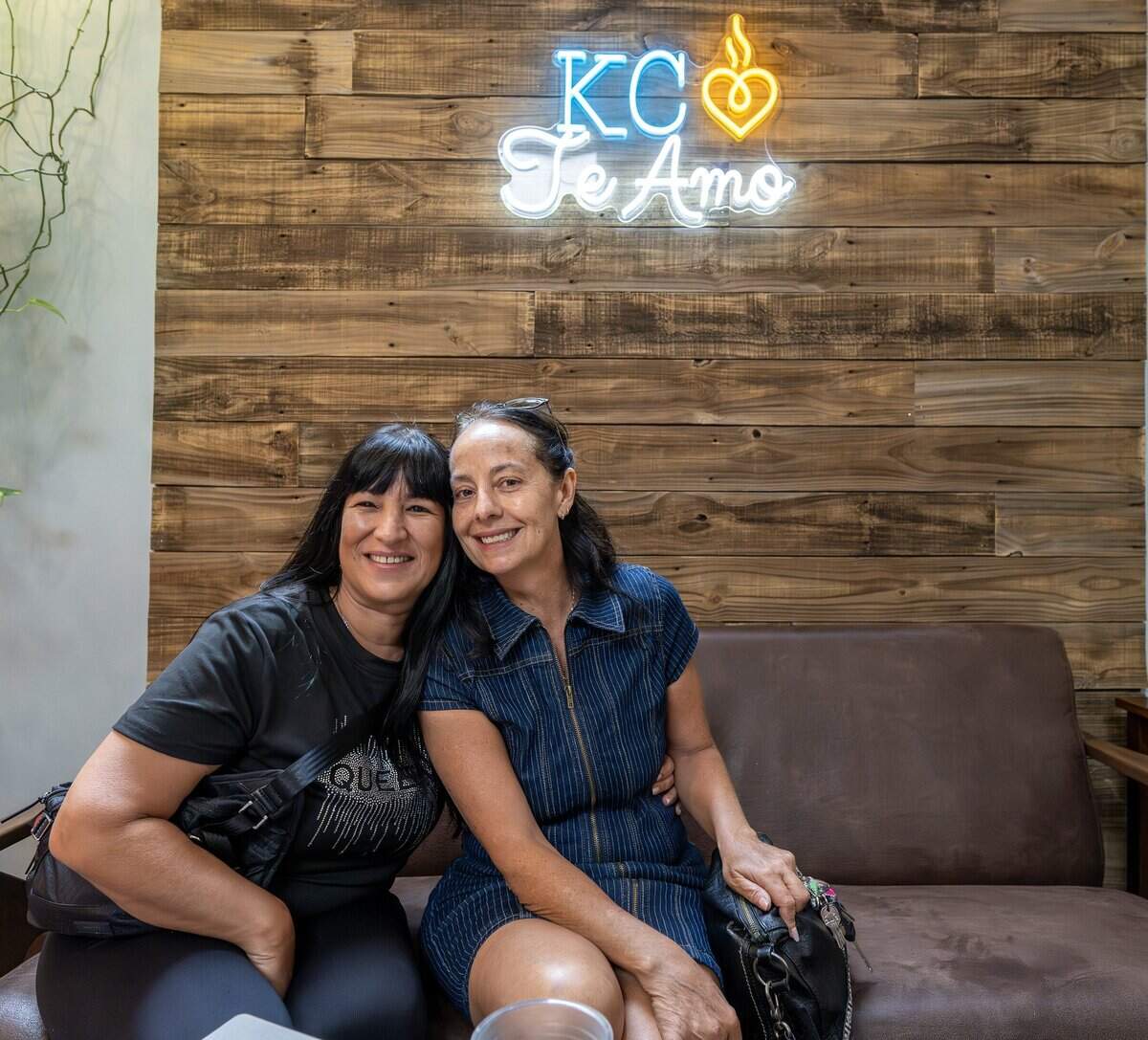 Natalia Testa, left, an artist from Buenos Aires, Argentina, and her cousin Miel Castagna-Herrera, co-owner of Café Corazón, pose for a portrait beneath an illuminated neon sign at the Crossroads location of Café Corazón on Wednesday, June 24, 2026, in Kansas City.