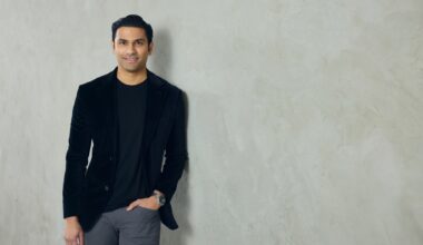 A well-dressed man leans against a neutral colored wall