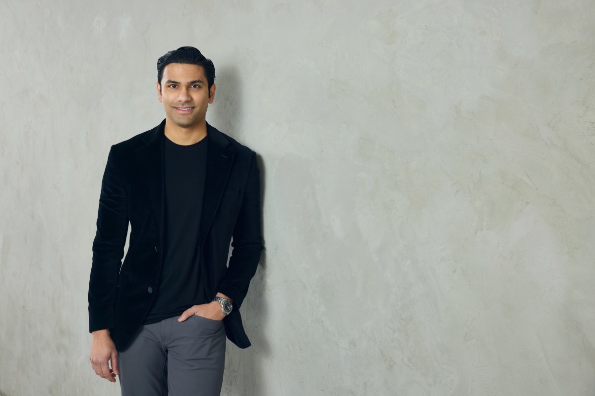 A well-dressed man leans against a neutral colored wall