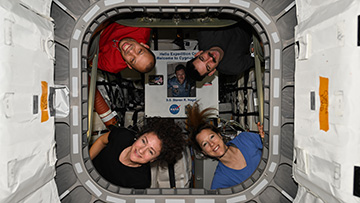 Crew of astronauts peering through spacecraft doorway.