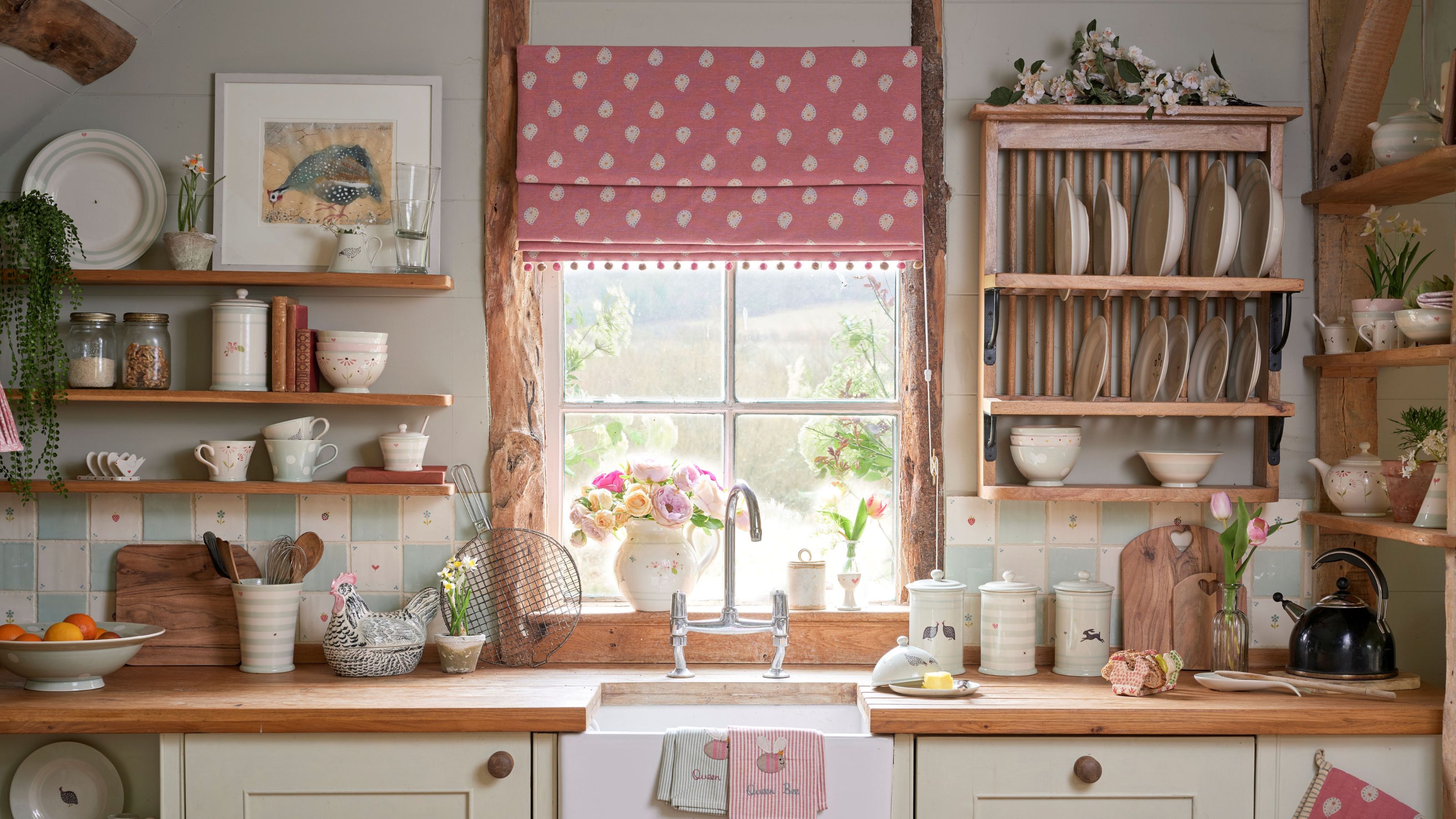 Kitchen sink beneath a window with a pink Roman blind, featuring wooden countertops, a farmhouse sink, and a wooden plate rack