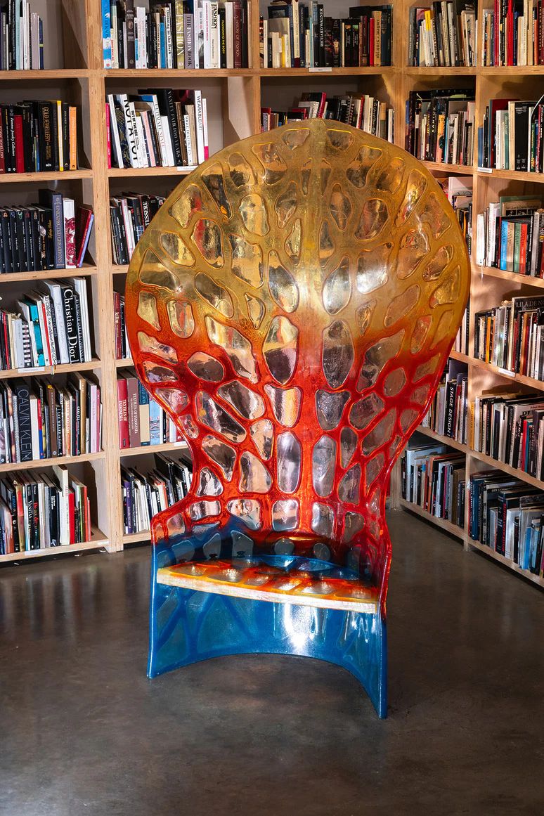 Colorful, translucent chair with web-like design in library setting surrounded by bookshelves.