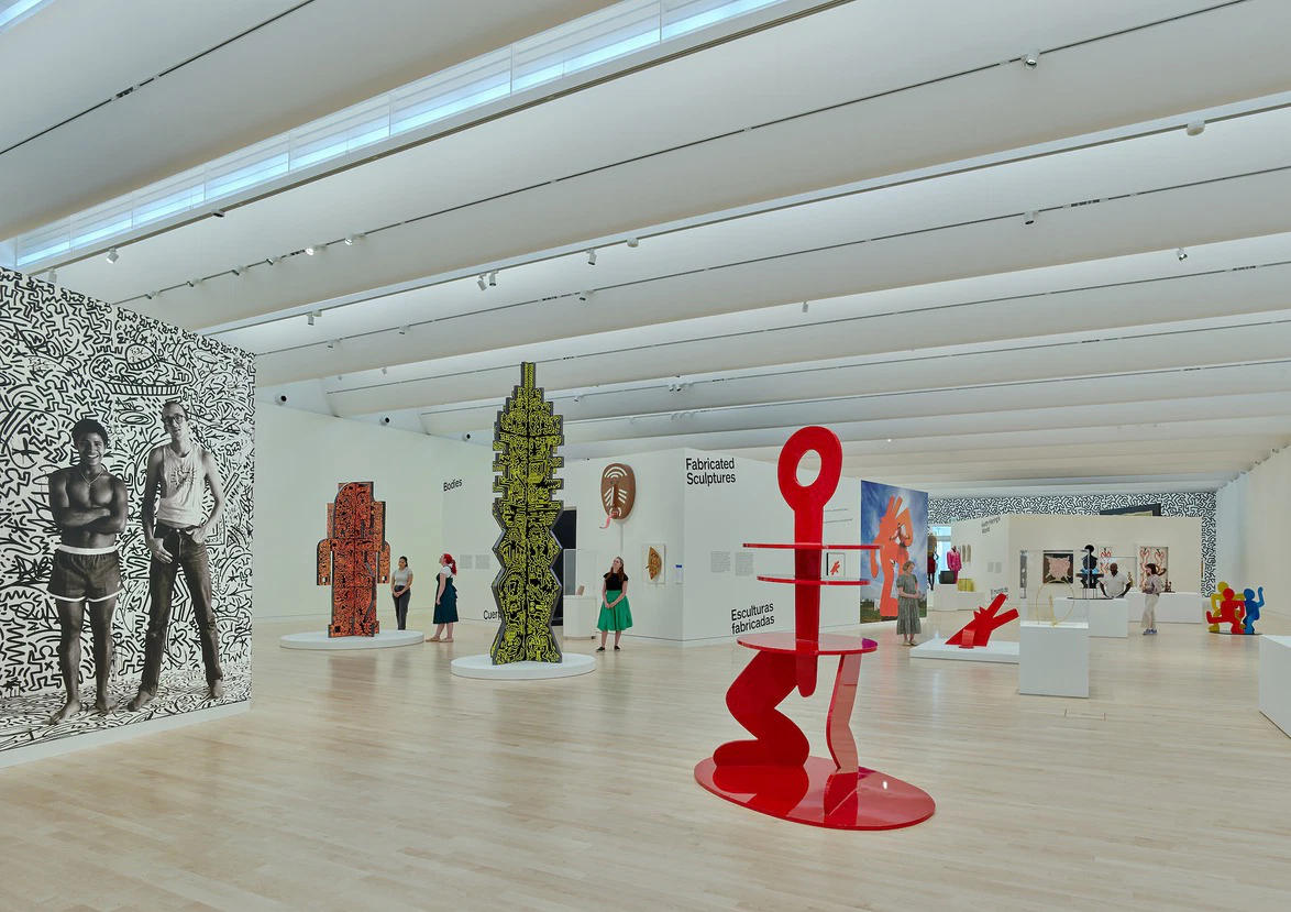 Contemporary art exhibition with colorful abstract sculptures and visitors exploring the gallery space with high ceilings.