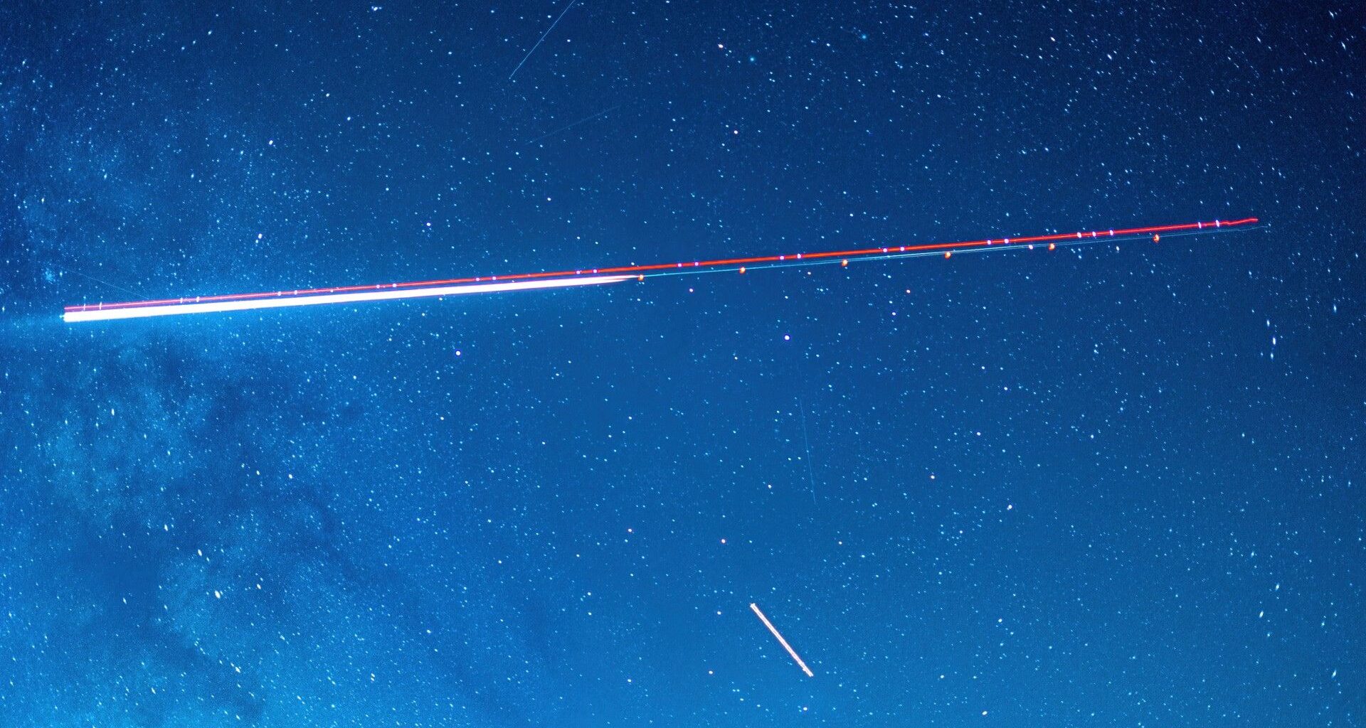 a long exposure photograph of the night sky captures the red and green lights of an aircraft as a pair of streaks among stars