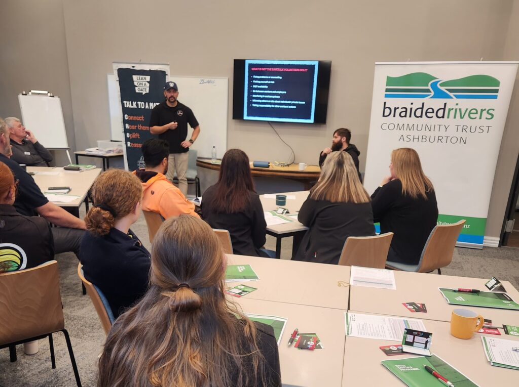 | Farmers Weekly Instructor presenting at the front of a classroom-style workshop, with a slide on a screen and a Braided Rivers banner nearby as attendees listen.
