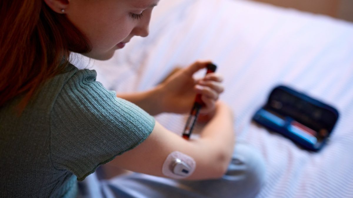 Close Up Of Diabetic Girl On Bed In At Home Using Insulin Pen To Measure To Check Blood Sugar Level