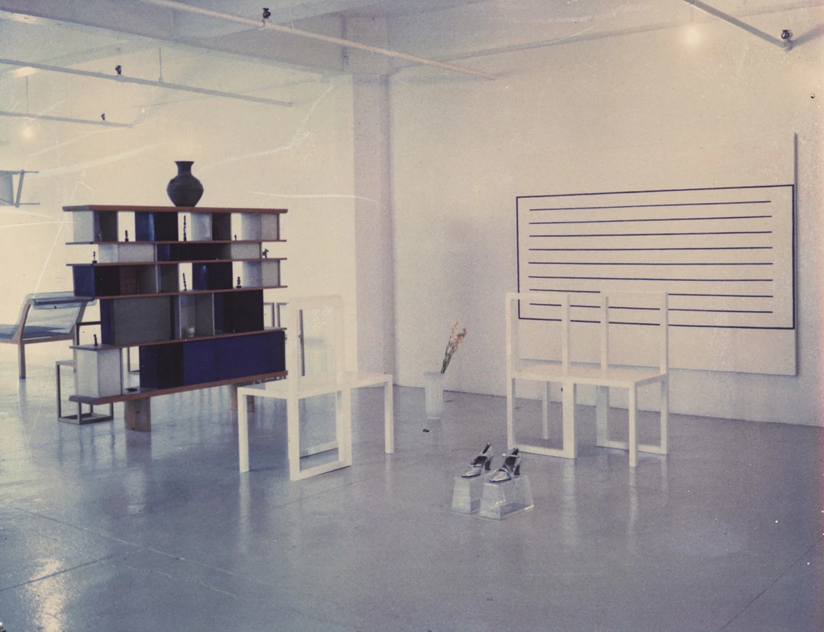Modern art installation in a gallery with abstract furniture, minimalist bookshelf, and geometric design elements.