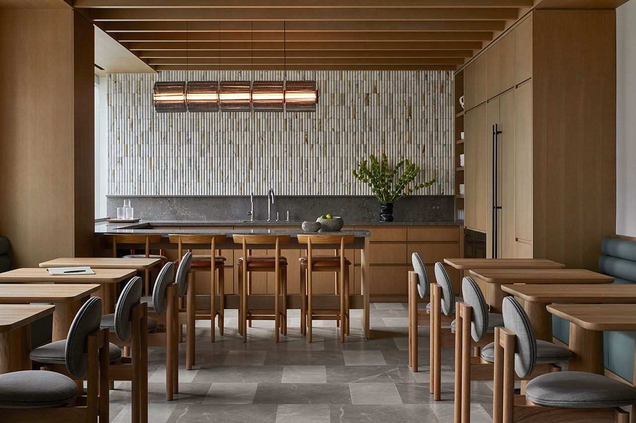 Modern dining area with wooden tables and chairs, a central kitchen island with bar stools, and a textured tile backsplash behind the counter.
