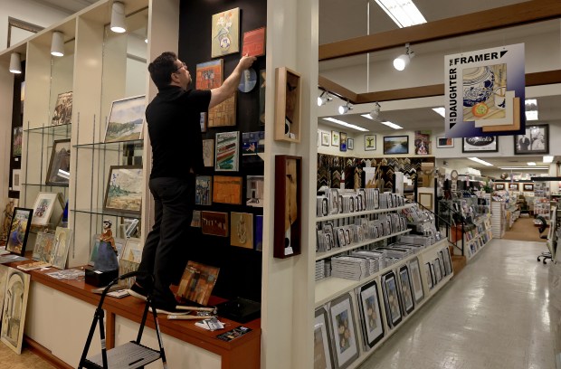 Corrick's Stationary owner Keven Brown hangs paintings by Maurice Lapp, Wednesday, June 17, 2026, in Santa Rosa. (Kent Porter / The Press Democrat)