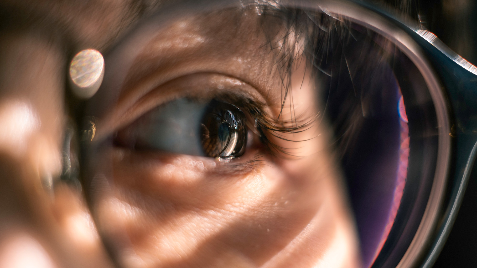 A close up of a person's brown eye behind the lens of the glasses.