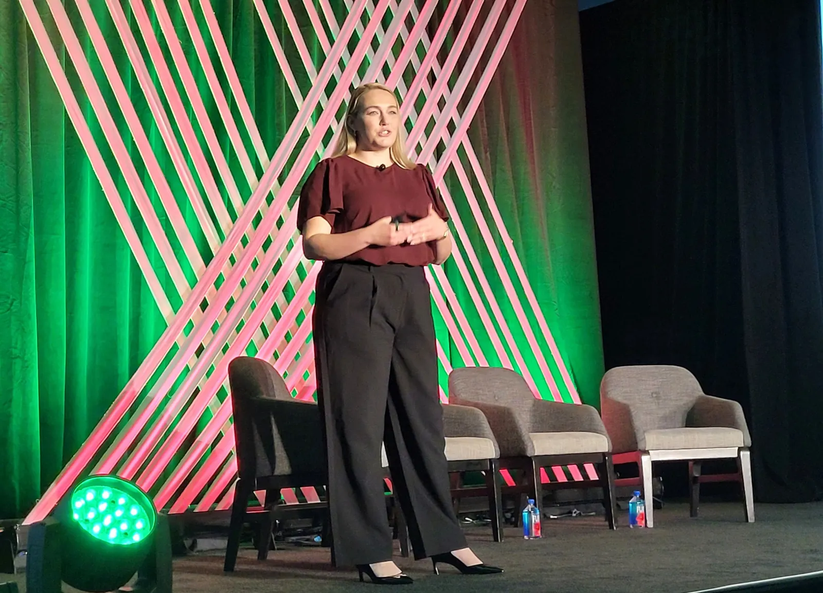 A person stands on stage in front of a green background while addressing an audience.