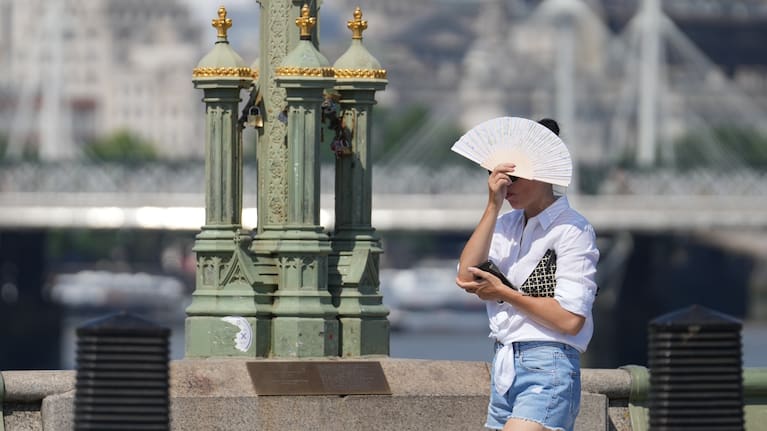A pedestrian tries to keep cool, using a fan to shelter form the sun as she walks over Westminster Bridge, in London.