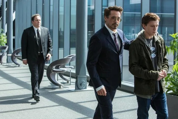 Three men in a modern office, one in a suit guiding another wearing casual clothes, with a third man following